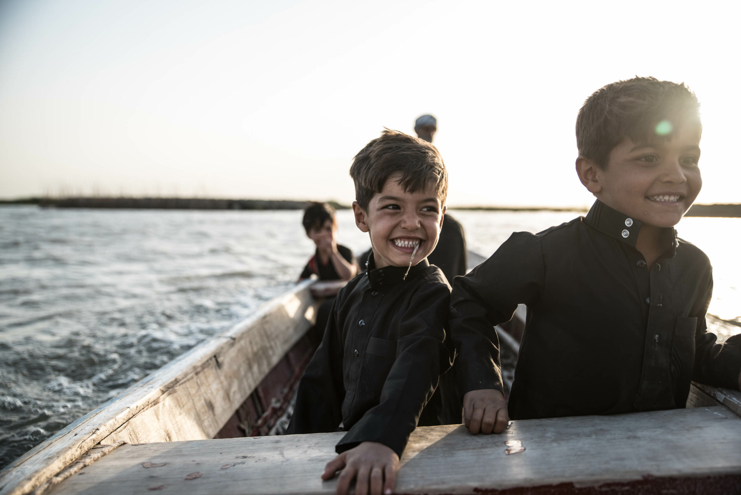 Muhammad and Shajjad wearing matching black dishdashas, happy in the boat, on their way to visit their uncle Hitham's new house.