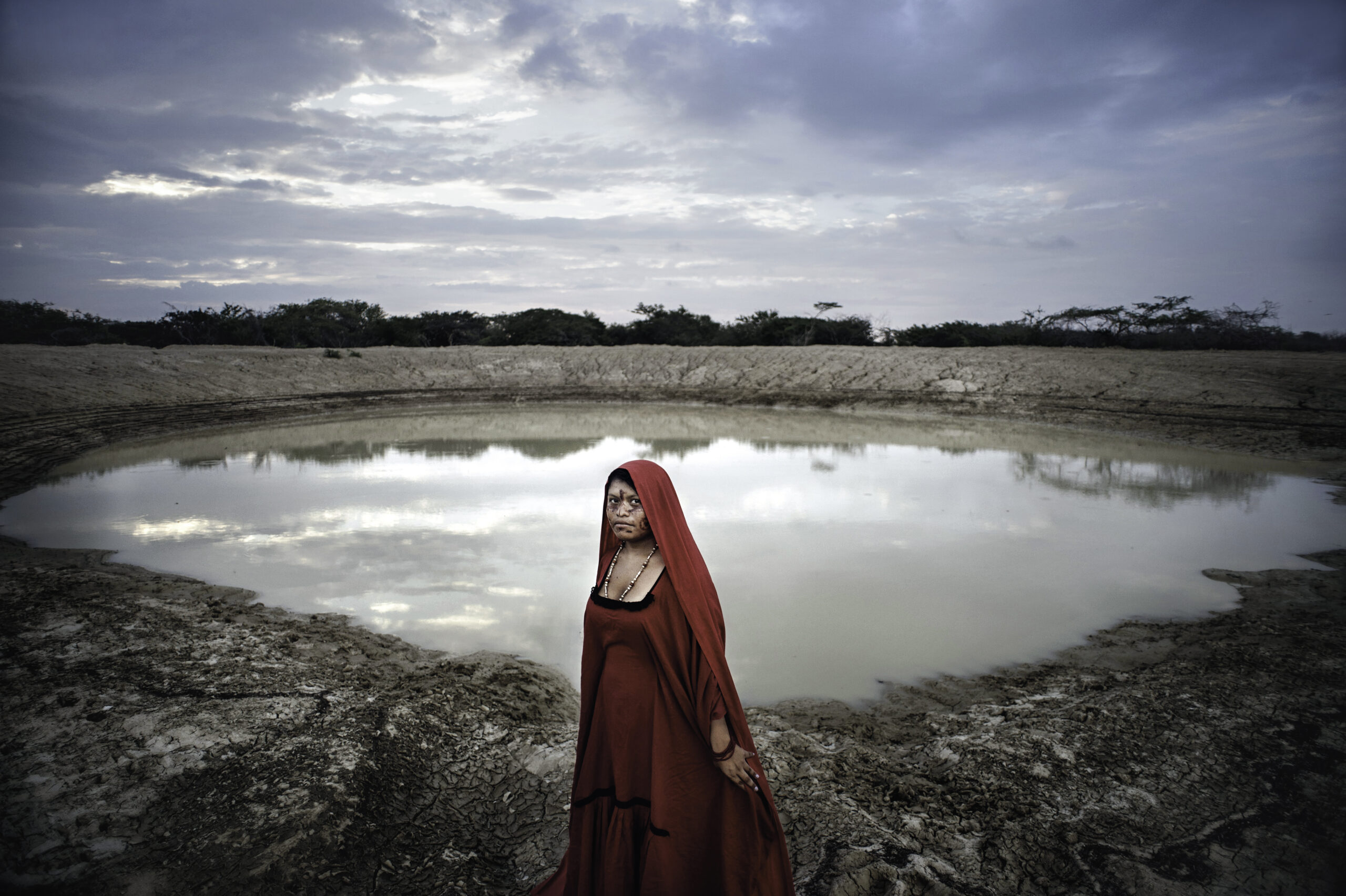 A Wayuu young woman poses in a traditional dress in front of the Jagüey of her community. This freshwater pool that is used to water the animals is a central element in each clan and has a strong symbolic power.